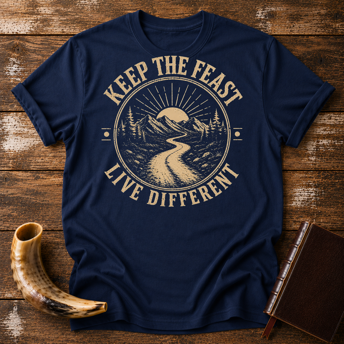 Navy t-shirt with KEEP THE FEAST LIVE DIFFERENT around a winding road toward a rising sun, laid flat with a shofar and a leather book
