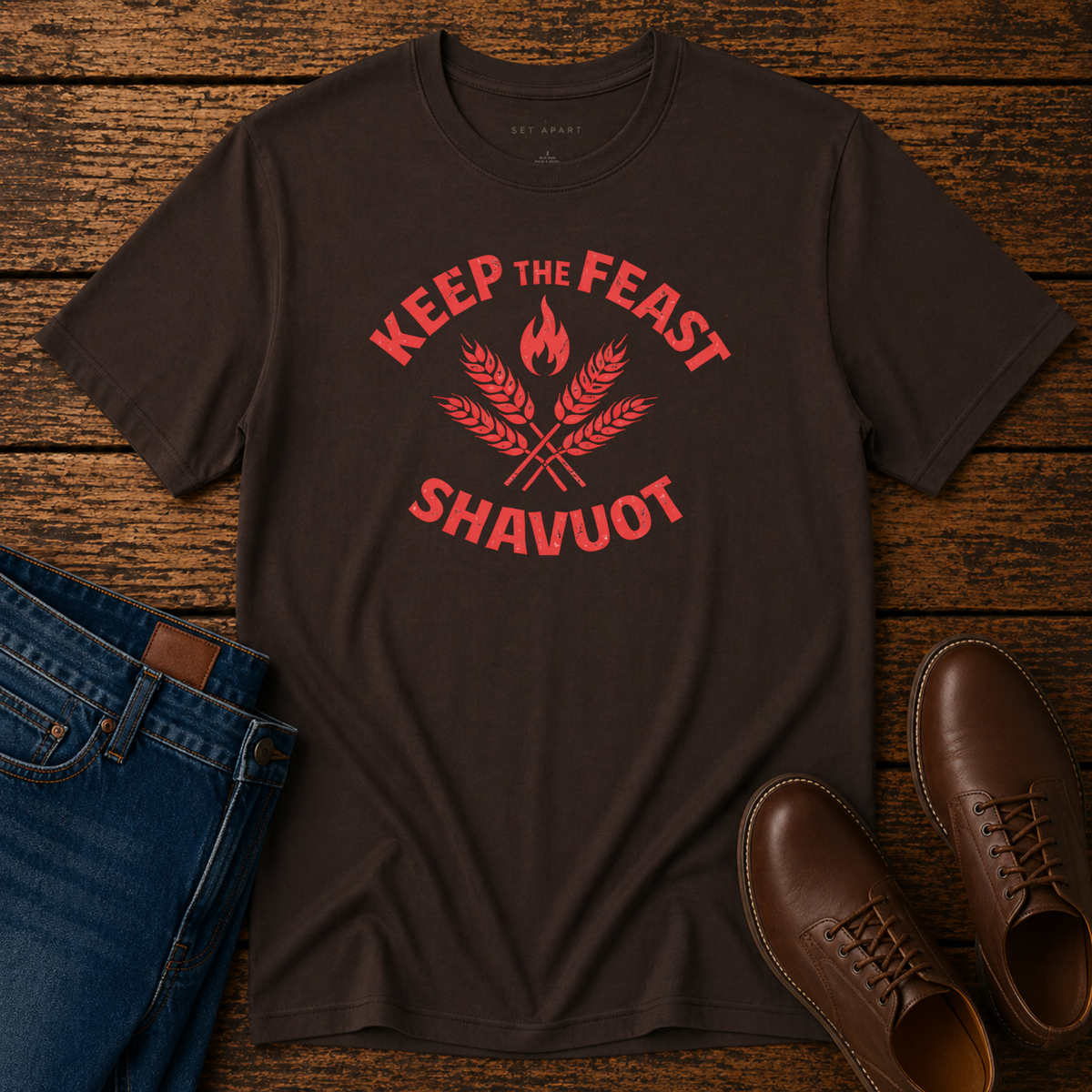 Dark chocolate Keep the Feast Shavuot tee with red wheat and flame design, laid flat with jeans and brown shoes