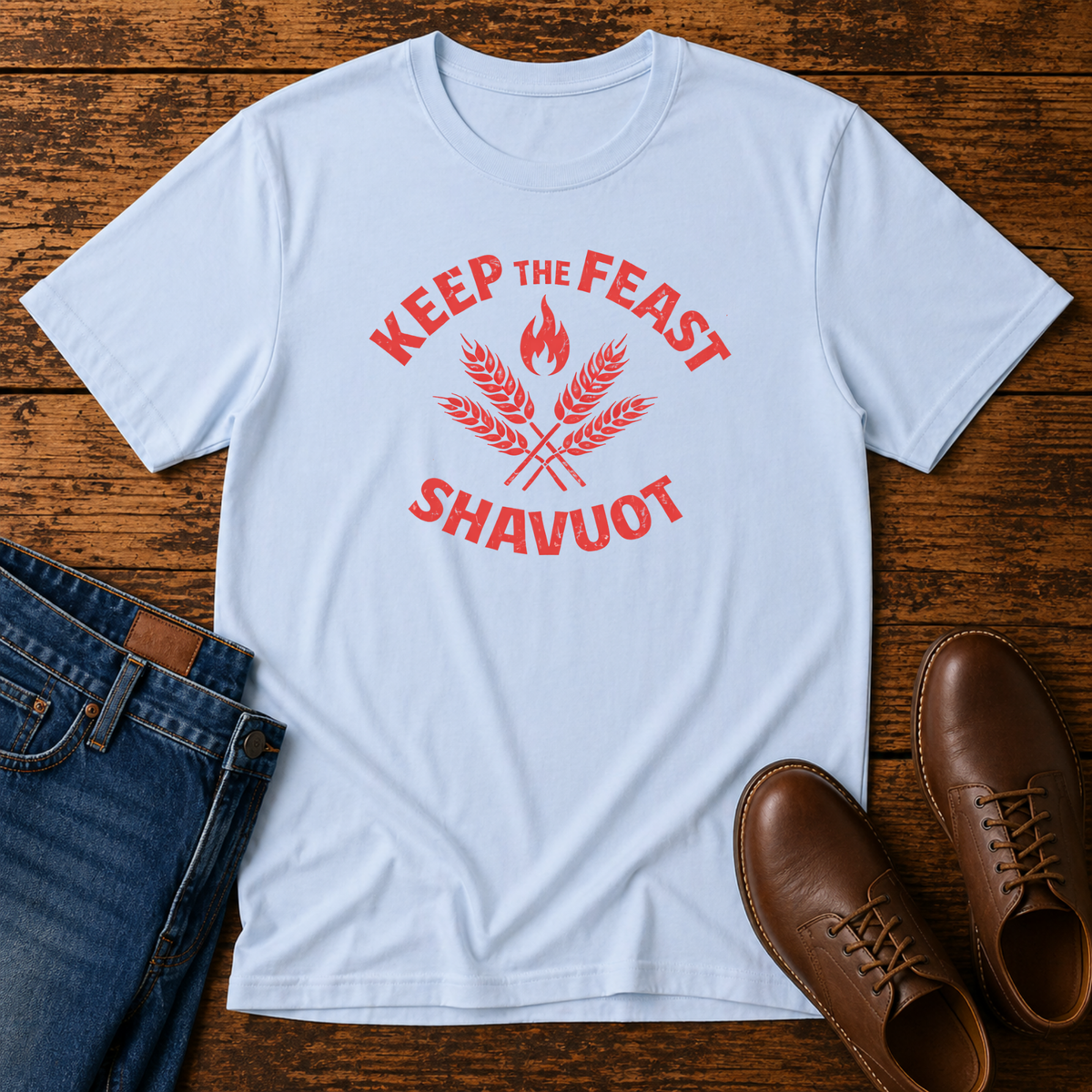 Light blue Keep the Feast Shavuot tee with red wheat and flame design, laid flat with jeans and brown shoes