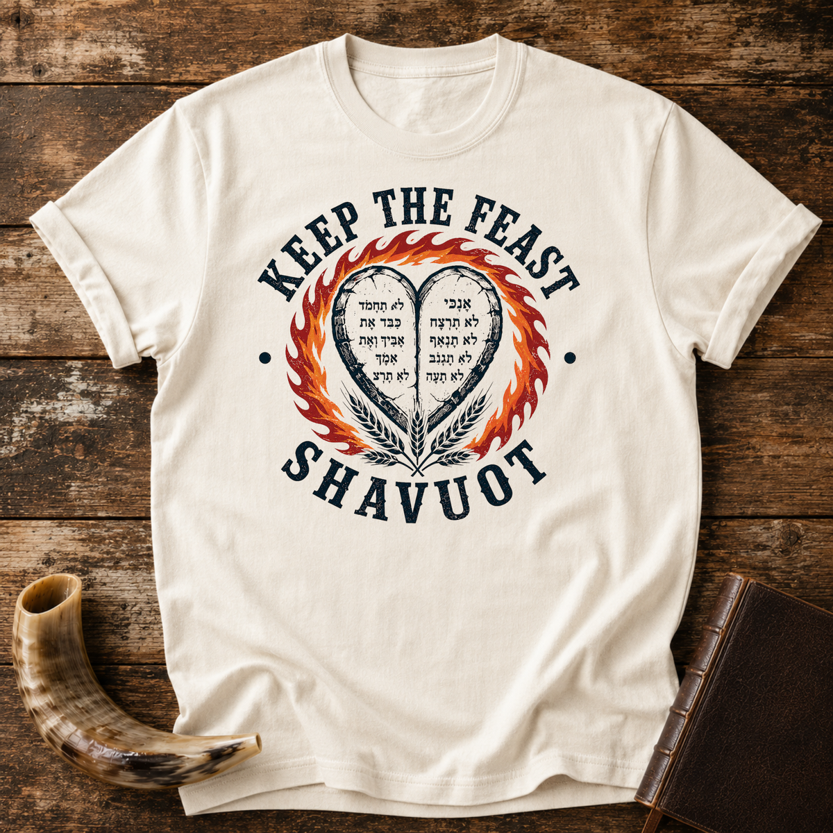 Natural cream t-shirt with KEEP THE FEAST SHAVUOT, Hebrew-lettered heart tablets, fire and wheat, laid flat with a shofar and a leather book