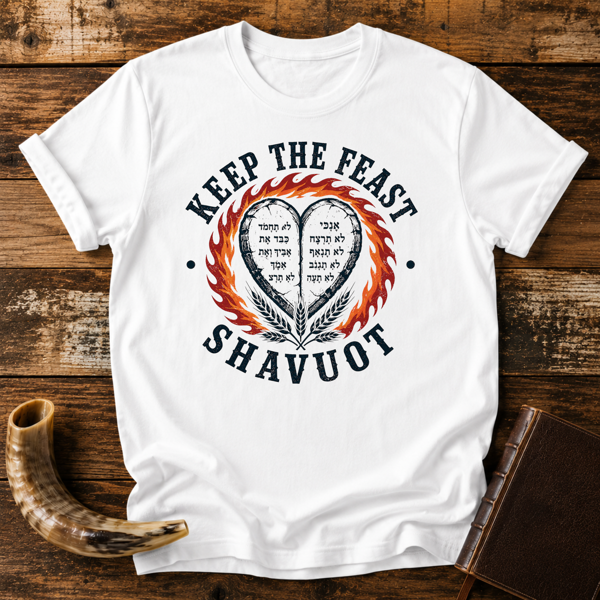 White t-shirt with KEEP THE FEAST SHAVUOT, Hebrew-lettered heart tablets, fire and wheat, laid flat with a shofar and a leather book
