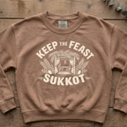 Espresso Keep the Feast SUKKOT sweatshirt with a sukkah framed by palm branches, laid flat on a wooden table