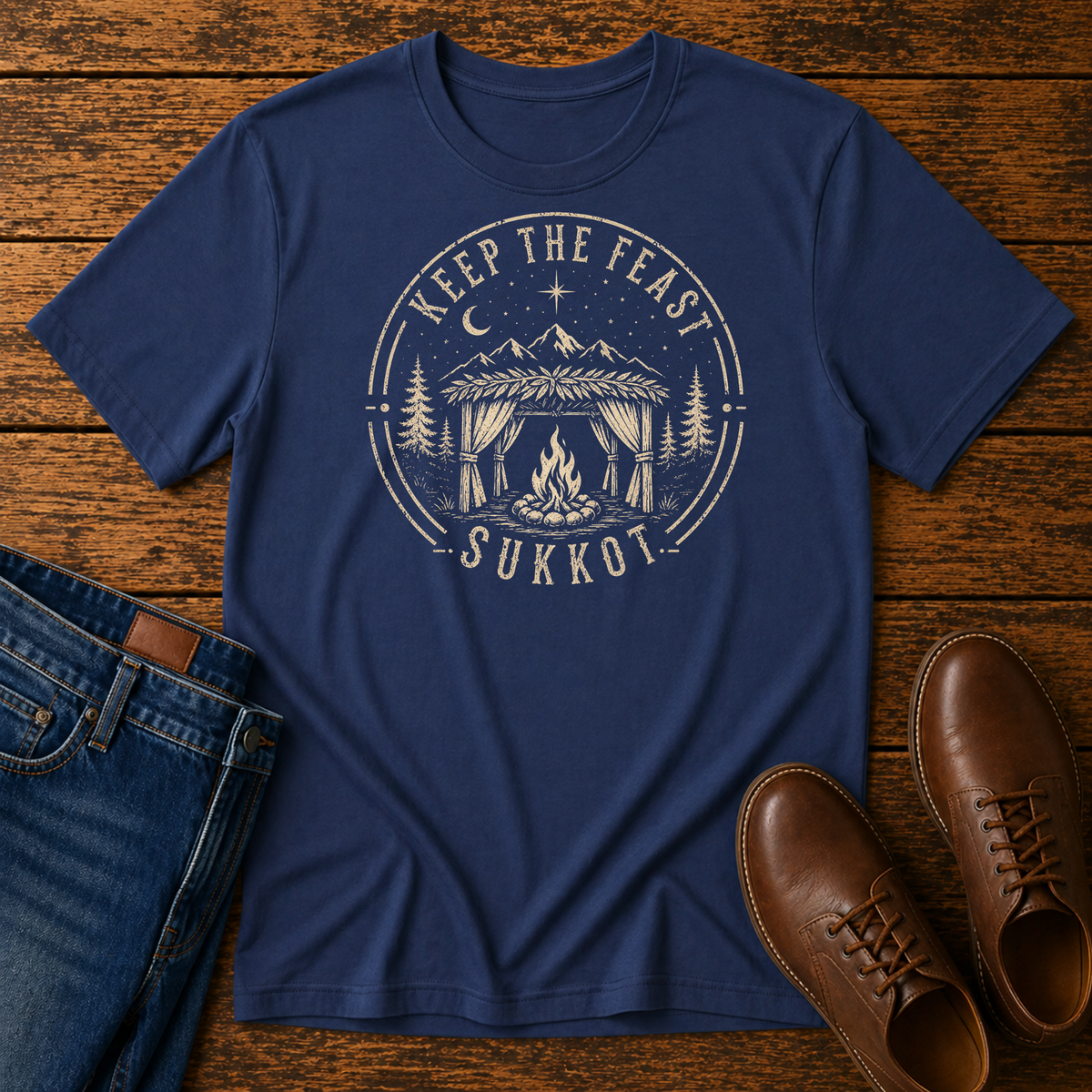 Navy t-shirt with a cream KEEP THE FEAST SUKKOT badge with a sukkah and campfire, laid flat with jeans and brown leather boots