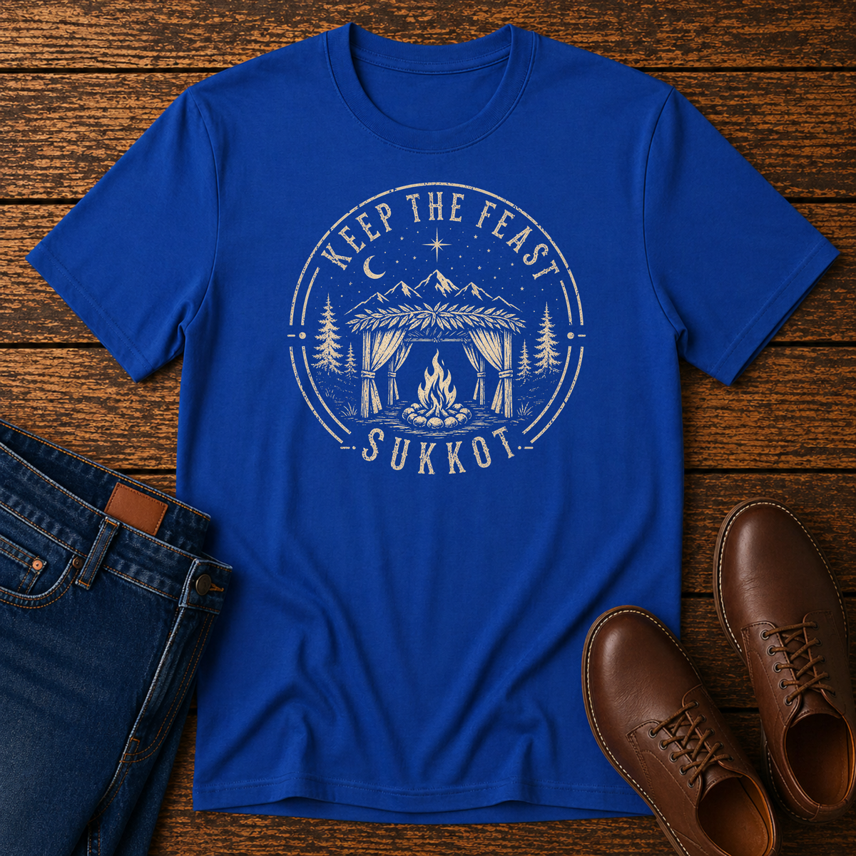 Royal blue t-shirt with a cream KEEP THE FEAST SUKKOT badge with a sukkah and campfire, laid flat with jeans and brown leather boots