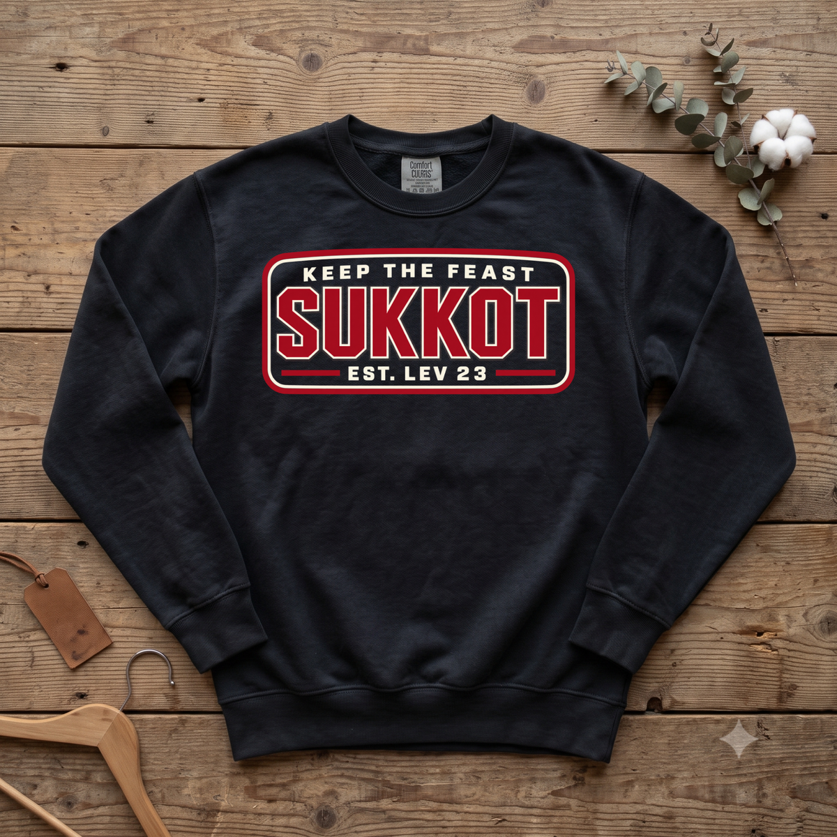 Black Keep the Feast SUKKOT Est. Lev 23 sweatshirt with a red badge design, laid flat on a wooden table