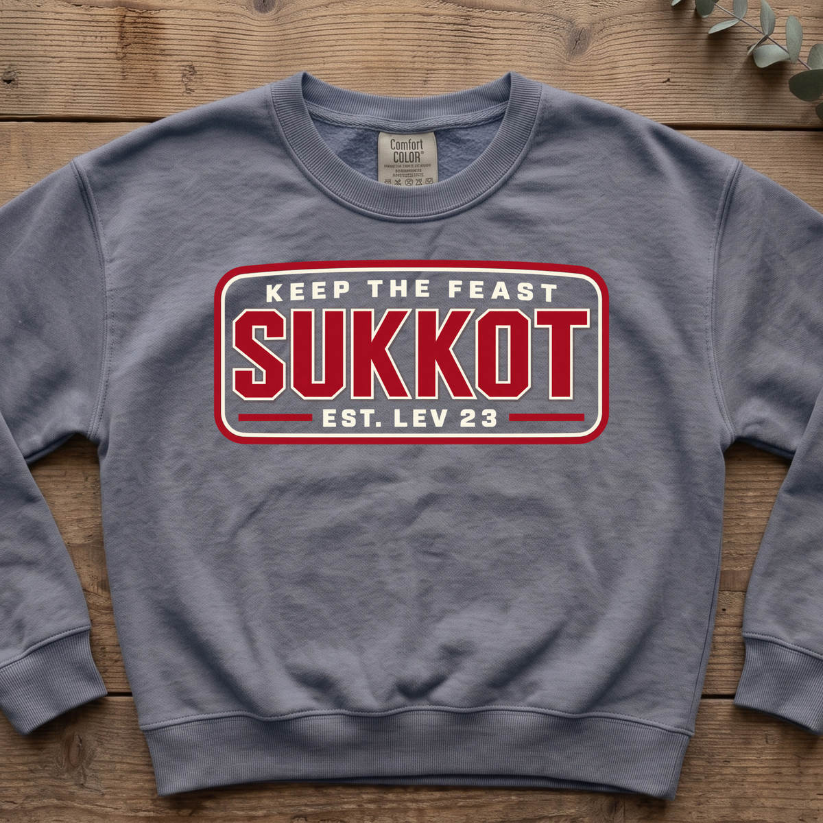Blue jean Keep the Feast SUKKOT Est. Lev 23 sweatshirt with a red badge design, laid flat on a wooden table