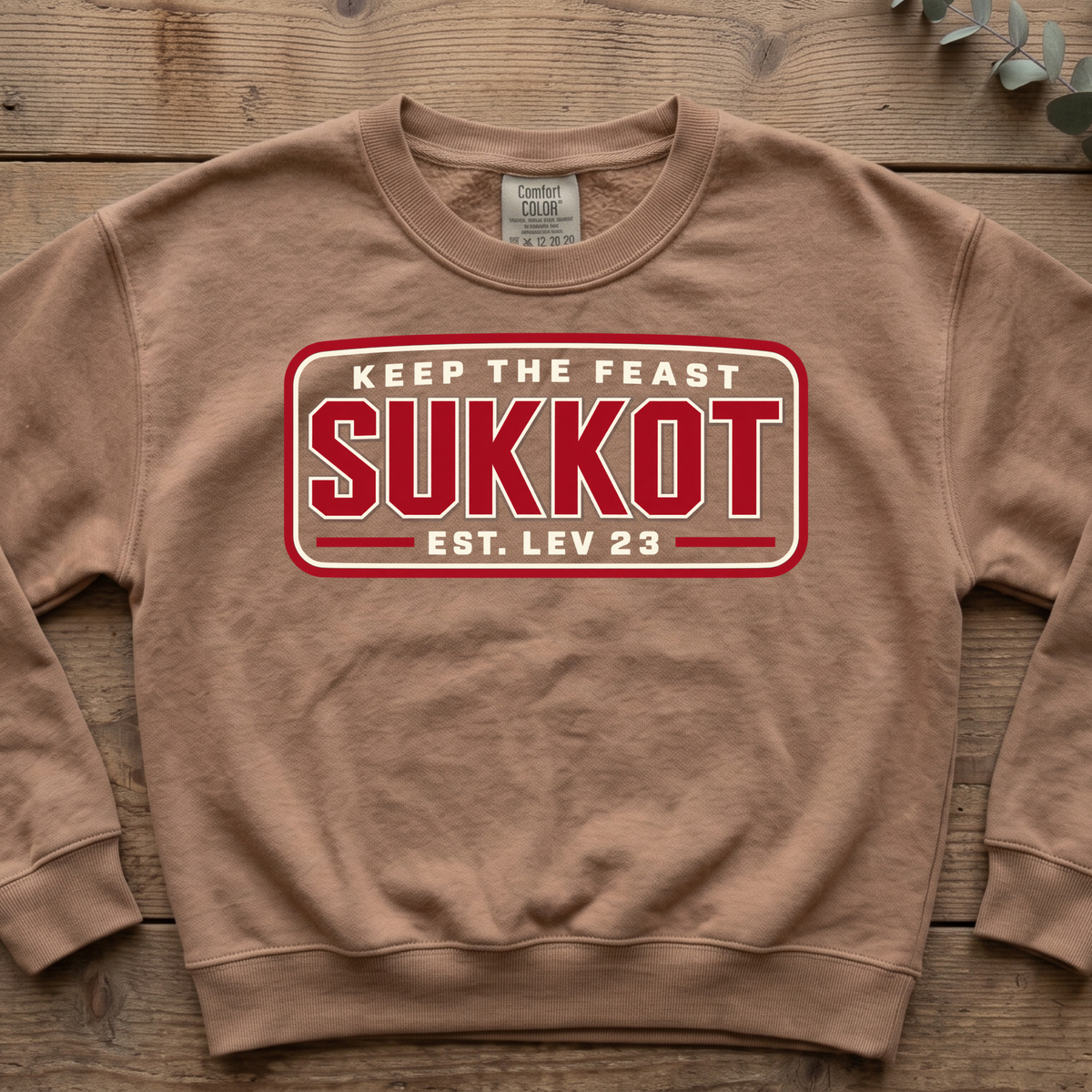 Espresso Keep the Feast SUKKOT Est. Lev 23 sweatshirt with a red badge design, laid flat on a wooden table