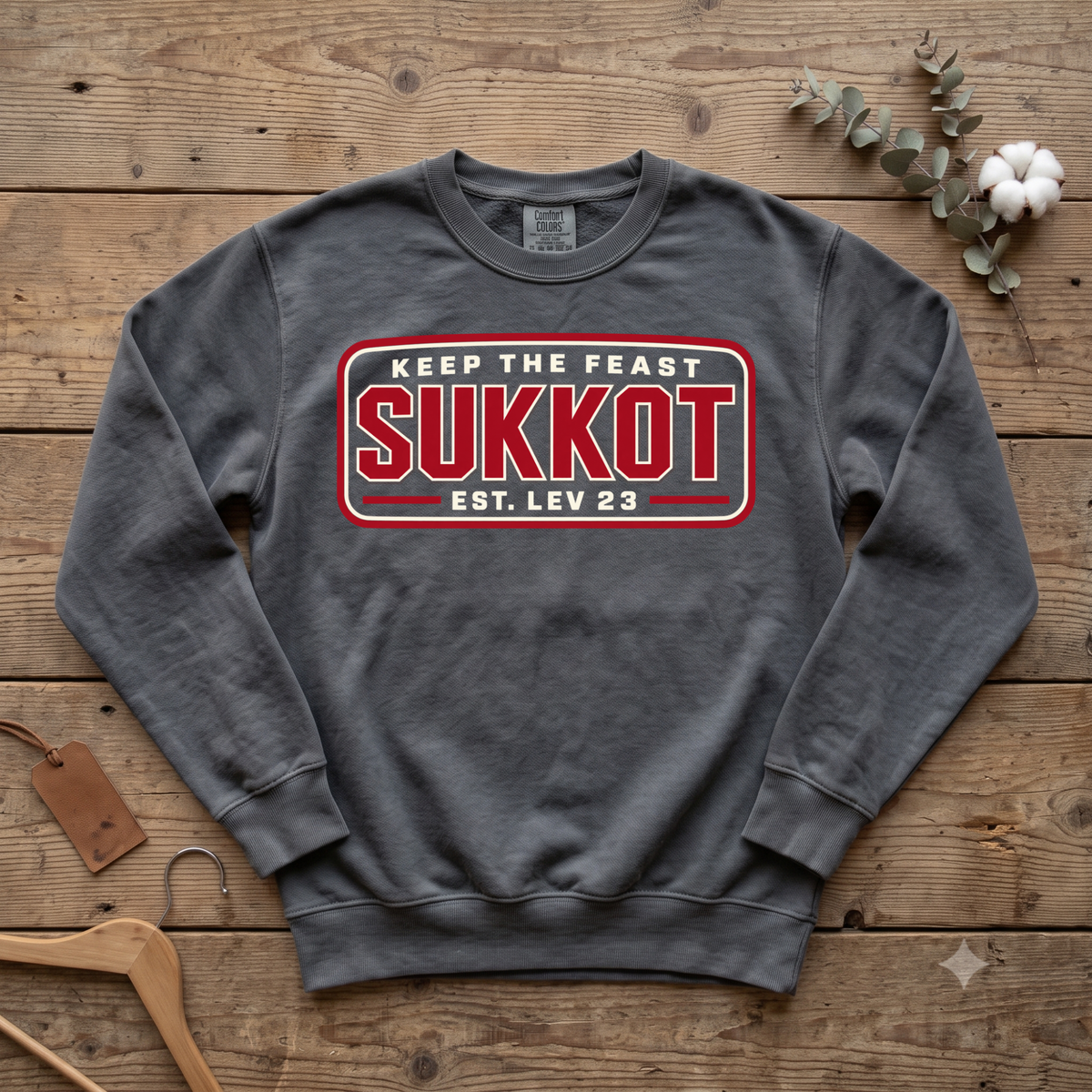 Pepper Keep the Feast SUKKOT Est. Lev 23 sweatshirt with a red badge design, laid flat on a wooden table