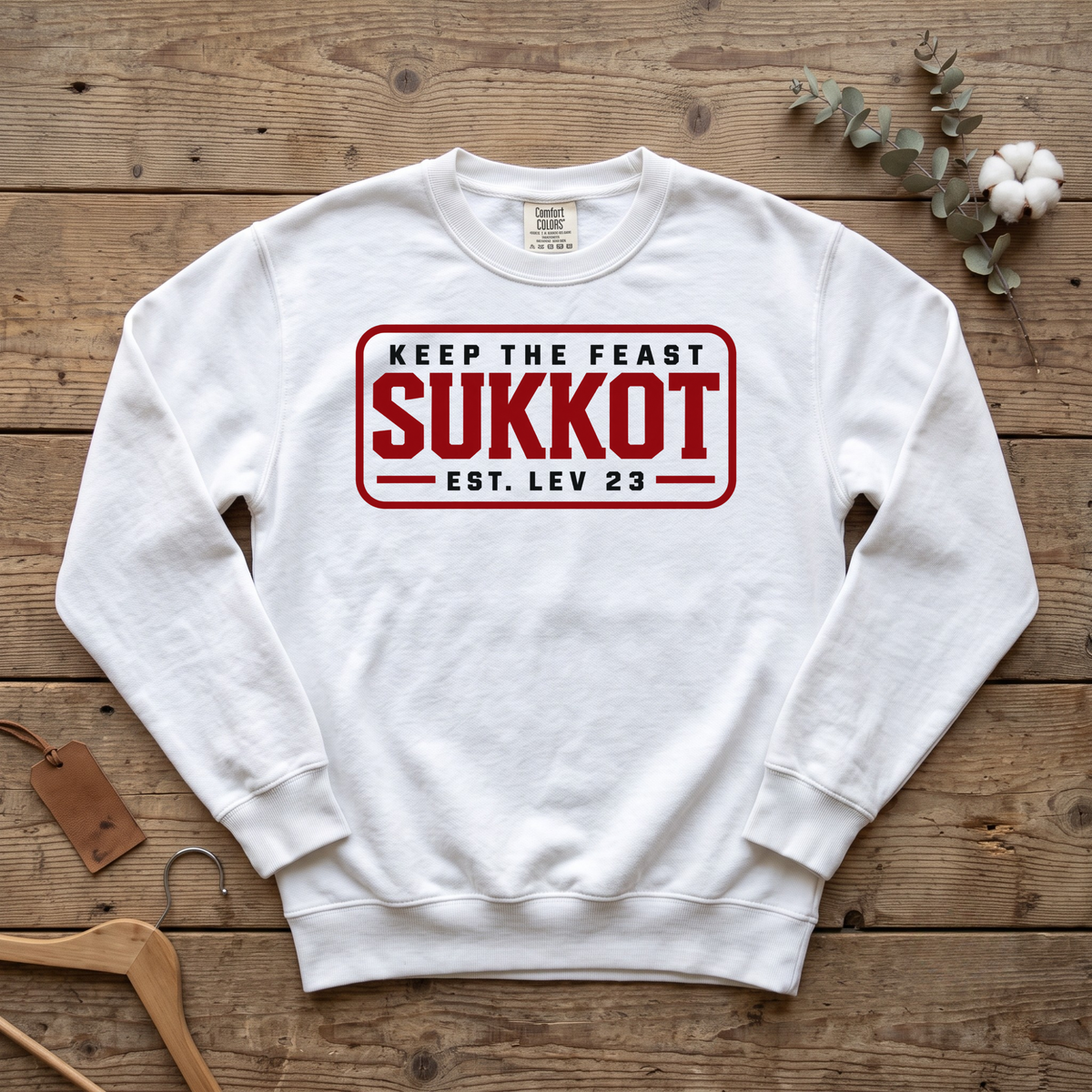 White Keep the Feast SUKKOT Est. Lev 23 sweatshirt with a red badge design, laid flat on a wooden table
