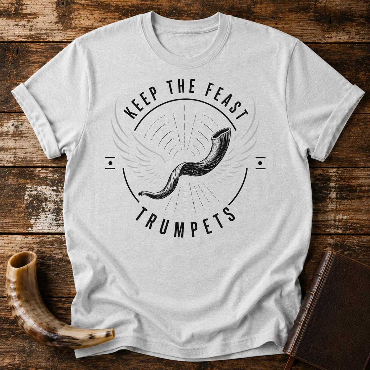Sport grey t-shirt with a winged shofar inside KEEP THE FEAST TRUMPETS, laid flat with a shofar and a leather book