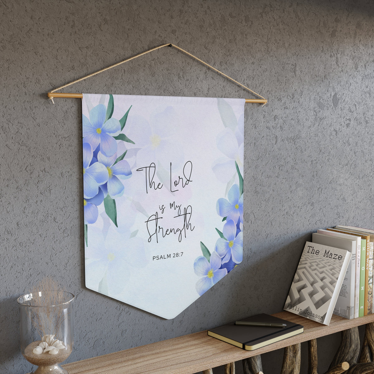 Light blue The Lord is my Strength wall pennant with watercolor blue flowers, Psalm 28:7, hanging on a gray wall above a bookshelf