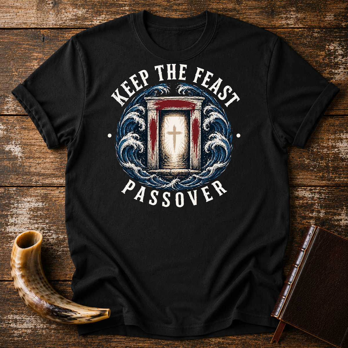 Black t-shirt with KEEP THE FEAST PASSOVER, a red-marked doorway with a cross and waves, laid flat with a shofar and a leather book