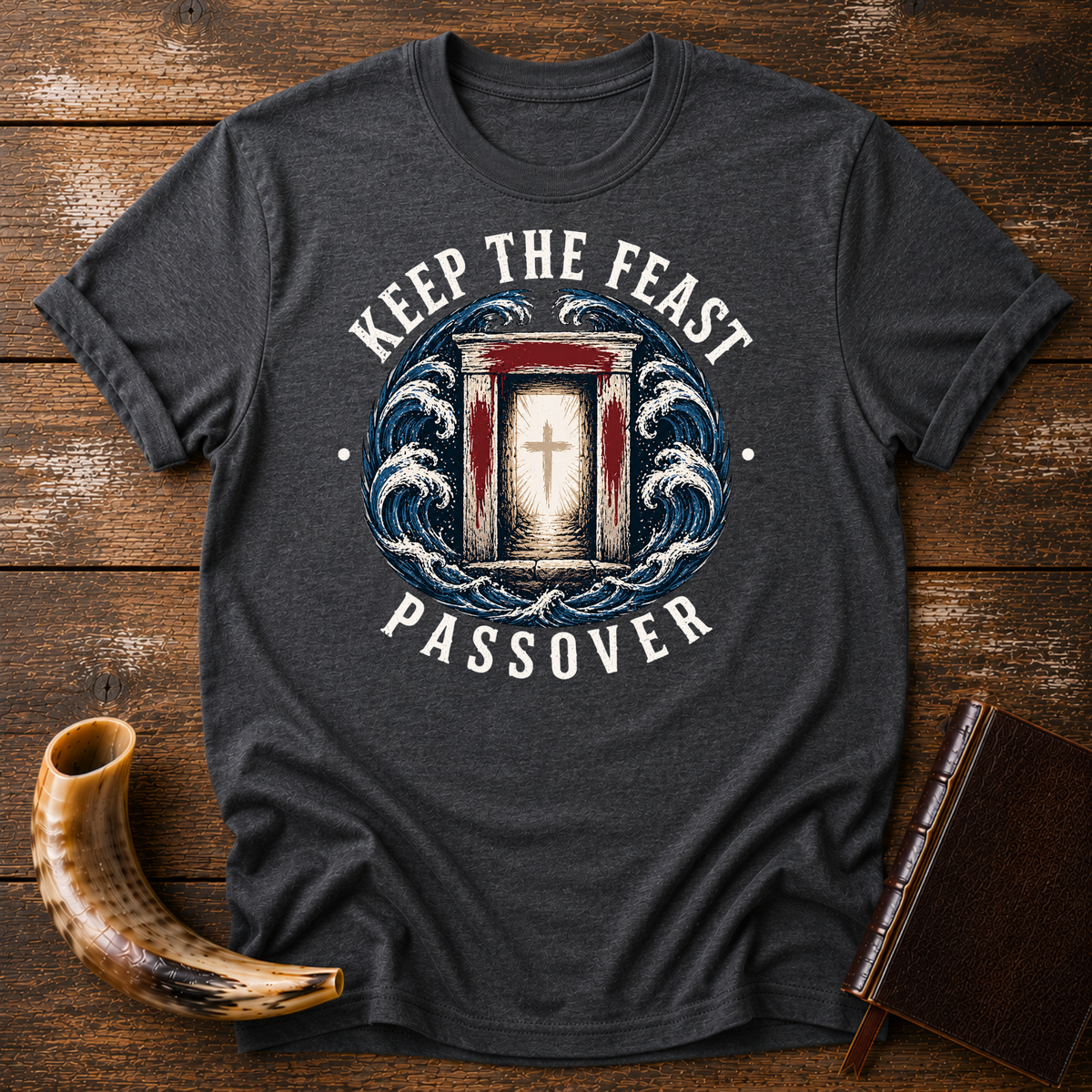 Dark heather gray t-shirt with KEEP THE FEAST PASSOVER, a red-marked doorway with a cross and waves, laid flat with a shofar and a leather book