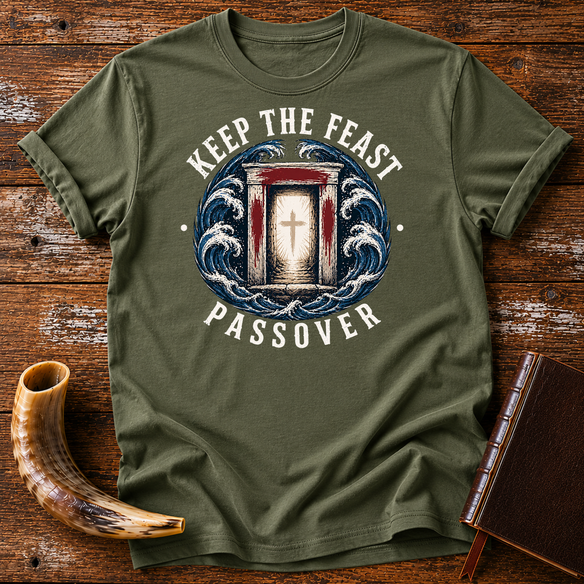 Military green t-shirt with KEEP THE FEAST PASSOVER, a red-marked doorway with a cross and waves, laid flat with a shofar and a leather book