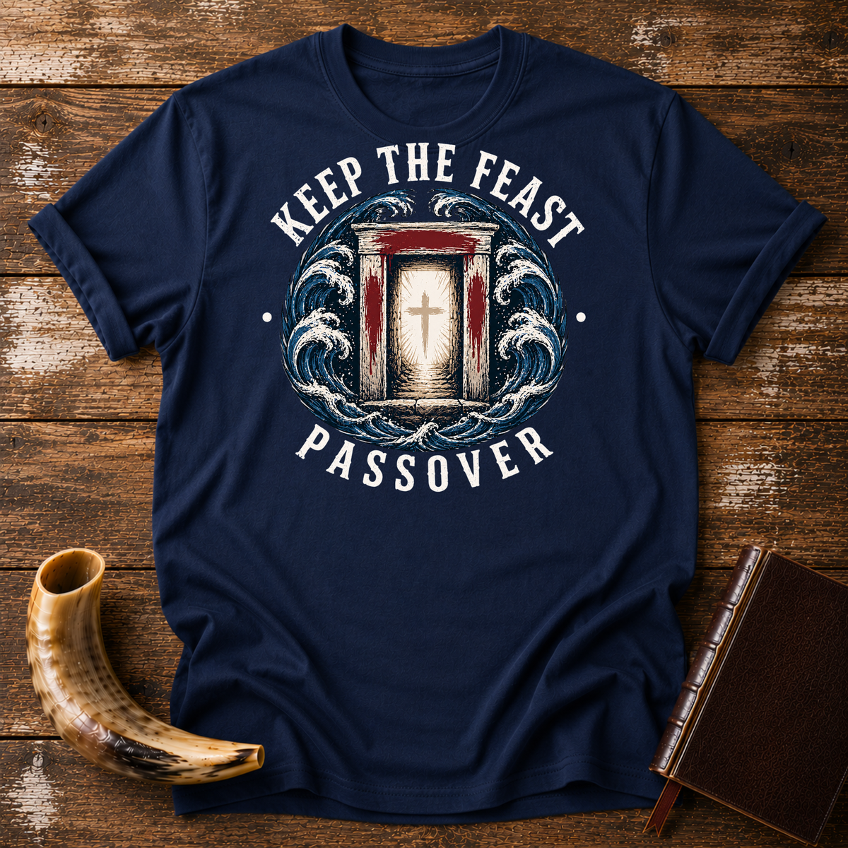 Navy t-shirt with KEEP THE FEAST PASSOVER, a red-marked doorway with a cross and waves, laid flat with a shofar and a leather book