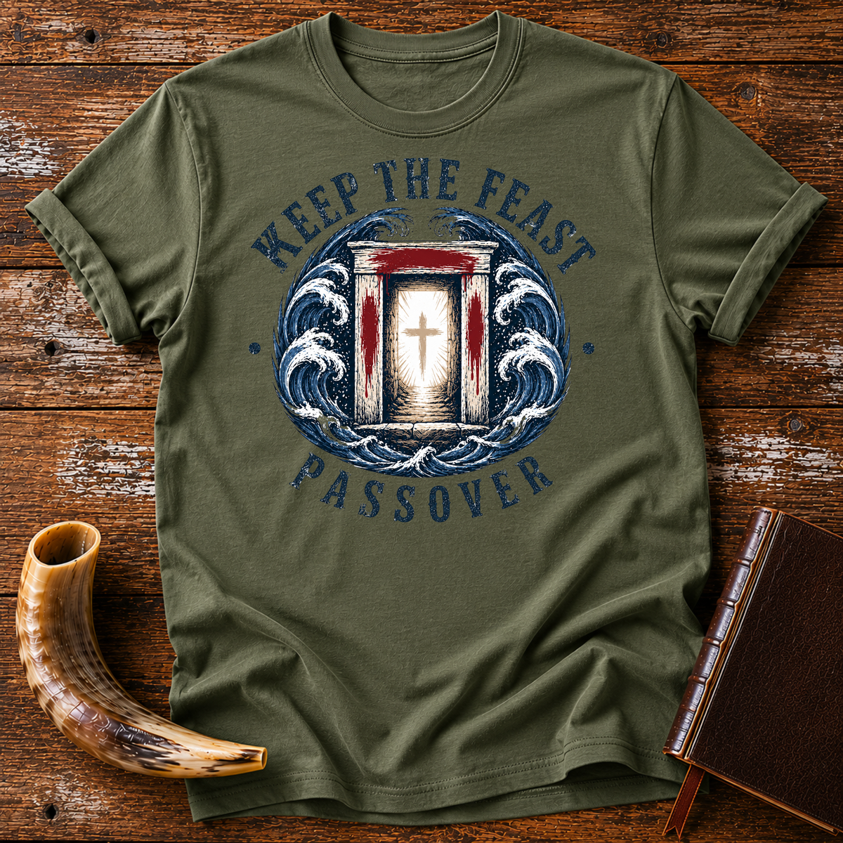 Military green t-shirt with KEEP THE FEAST PASSOVER, a red-marked doorway with a cross and waves, laid flat with a shofar and a leather book