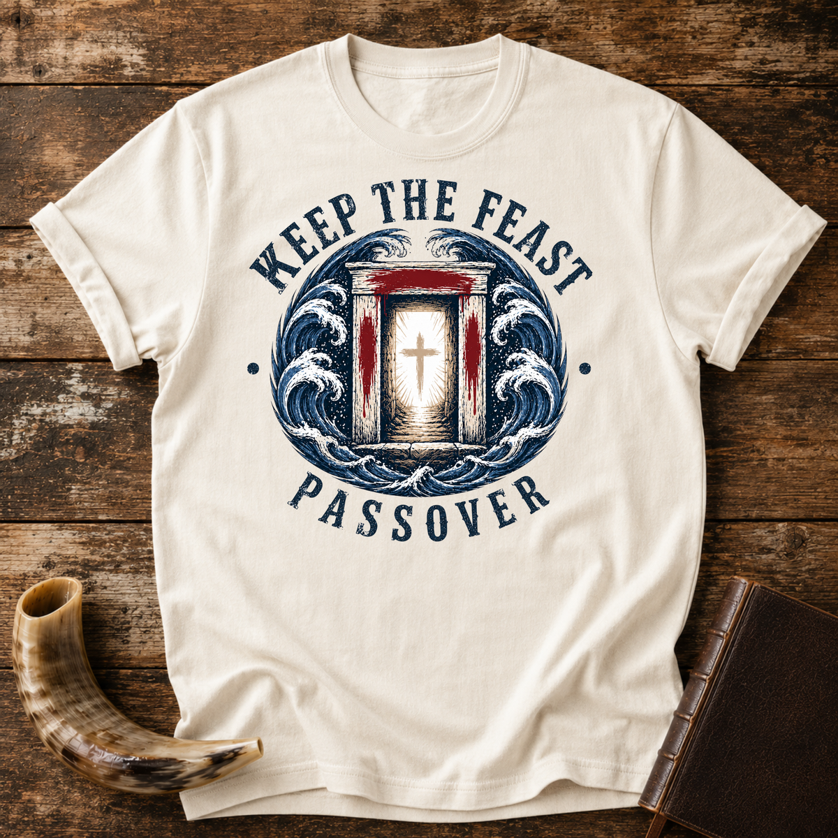 Natural cream t-shirt with KEEP THE FEAST PASSOVER, a red-marked doorway with a cross and waves, laid flat with a shofar and a leather book