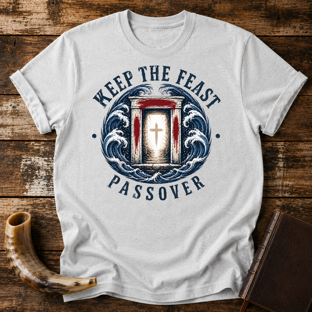 Sport grey t-shirt with KEEP THE FEAST PASSOVER, a red-marked doorway with a cross and waves, laid flat with a shofar and a leather book