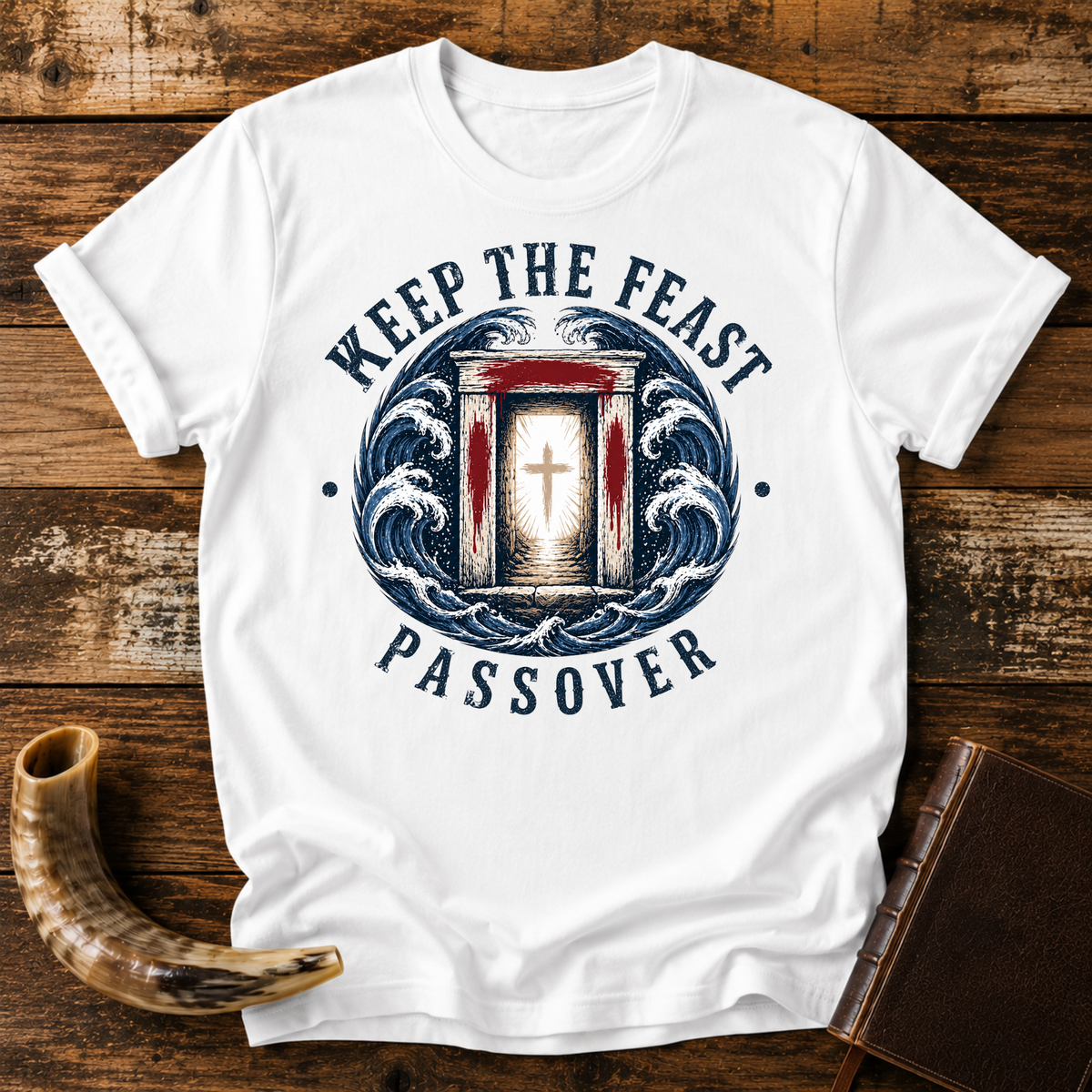 White t-shirt with KEEP THE FEAST PASSOVER, a red-marked doorway with a cross and waves, laid flat with a shofar and a leather book