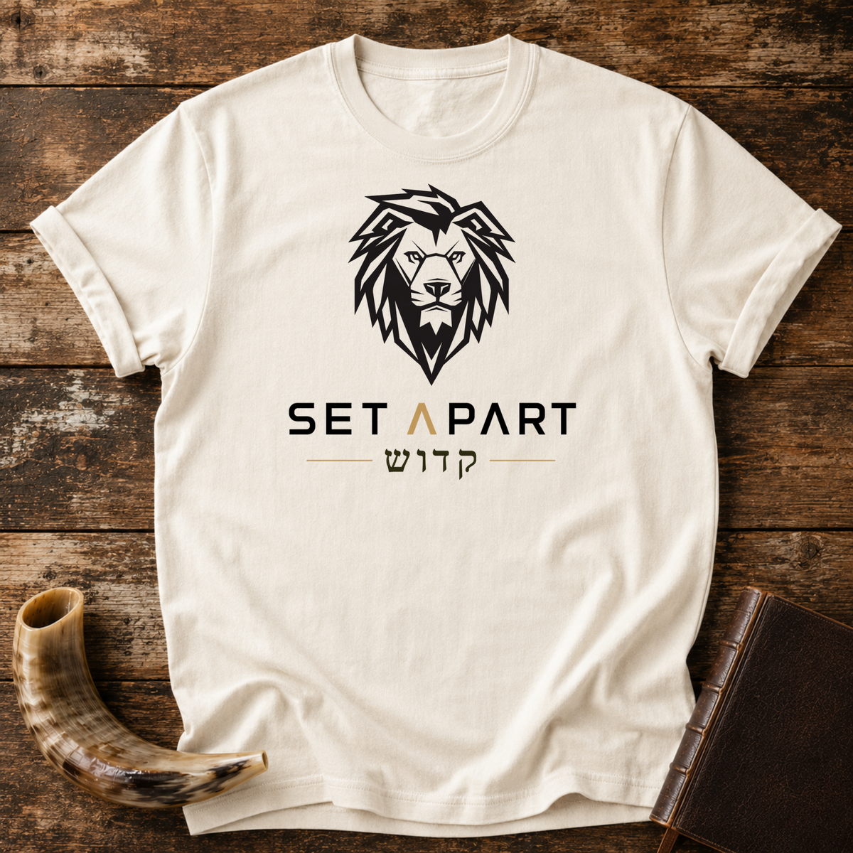 Natural cream t-shirt with a large black lion head above SET APART and Hebrew lettering, laid flat with a shofar and a leather book