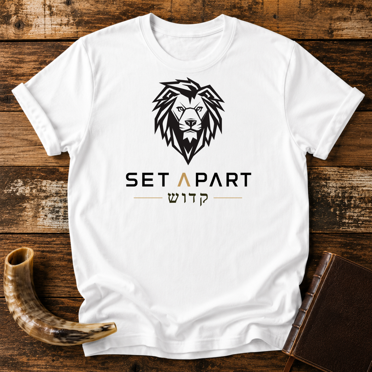 White t-shirt with a large black lion head above SET APART and Hebrew lettering, laid flat with a shofar and a leather book
