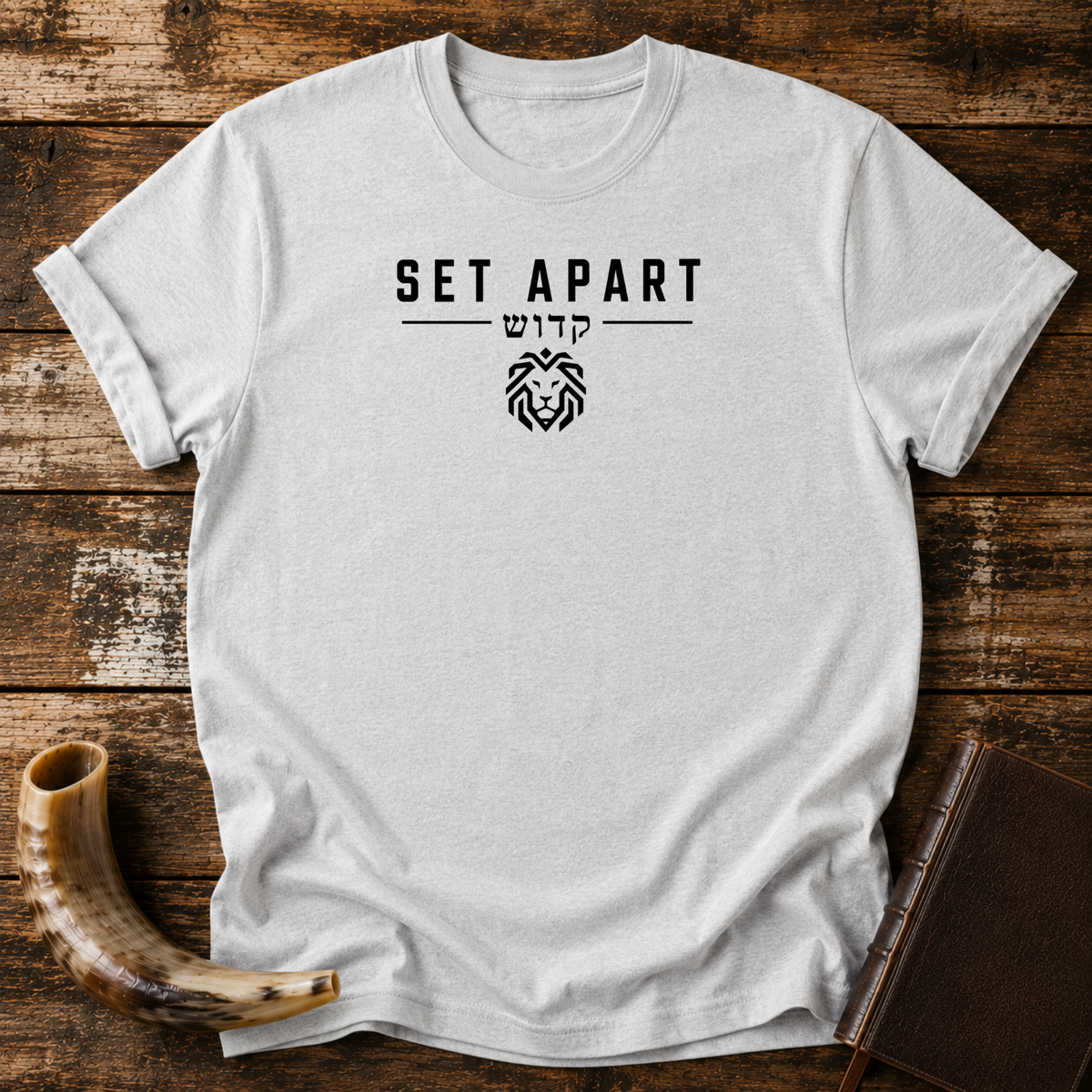 Sport grey t-shirt with SET APART, Hebrew lettering and a small geometric lion head, laid flat with a shofar and a leather book