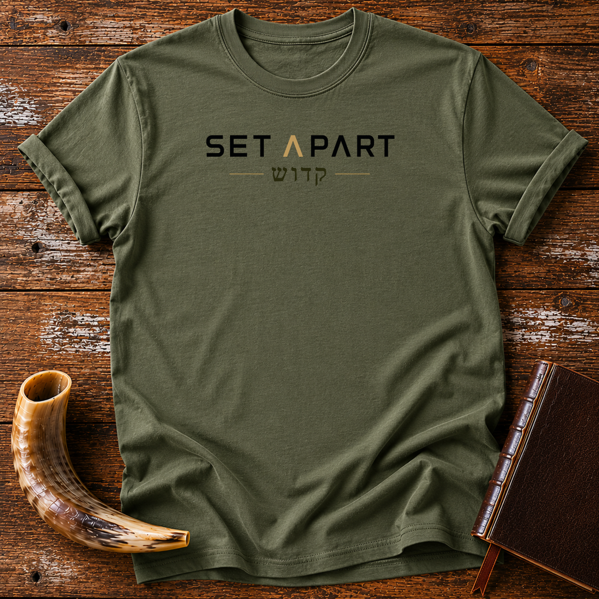Military green t-shirt with SET APART text in black and gold over a line of Hebrew lettering, laid flat with a shofar and a leather book