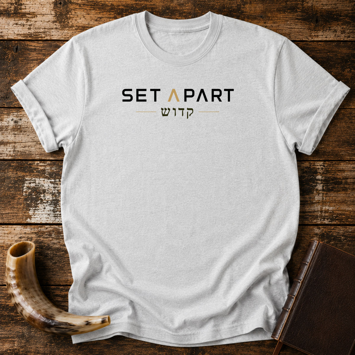 Sport grey t-shirt with SET APART text in black and gold over a line of Hebrew lettering, laid flat with a shofar and a leather book