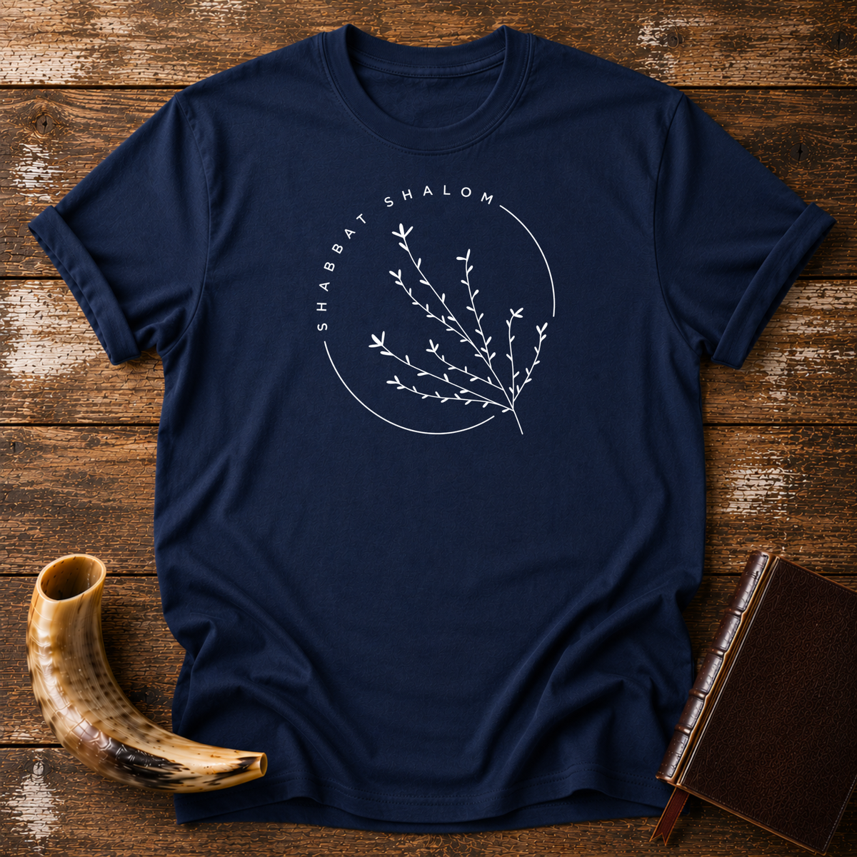 Navy t-shirt with a thin SHABBAT SHALOM circle around a delicate branch, laid flat with a shofar and a leather book