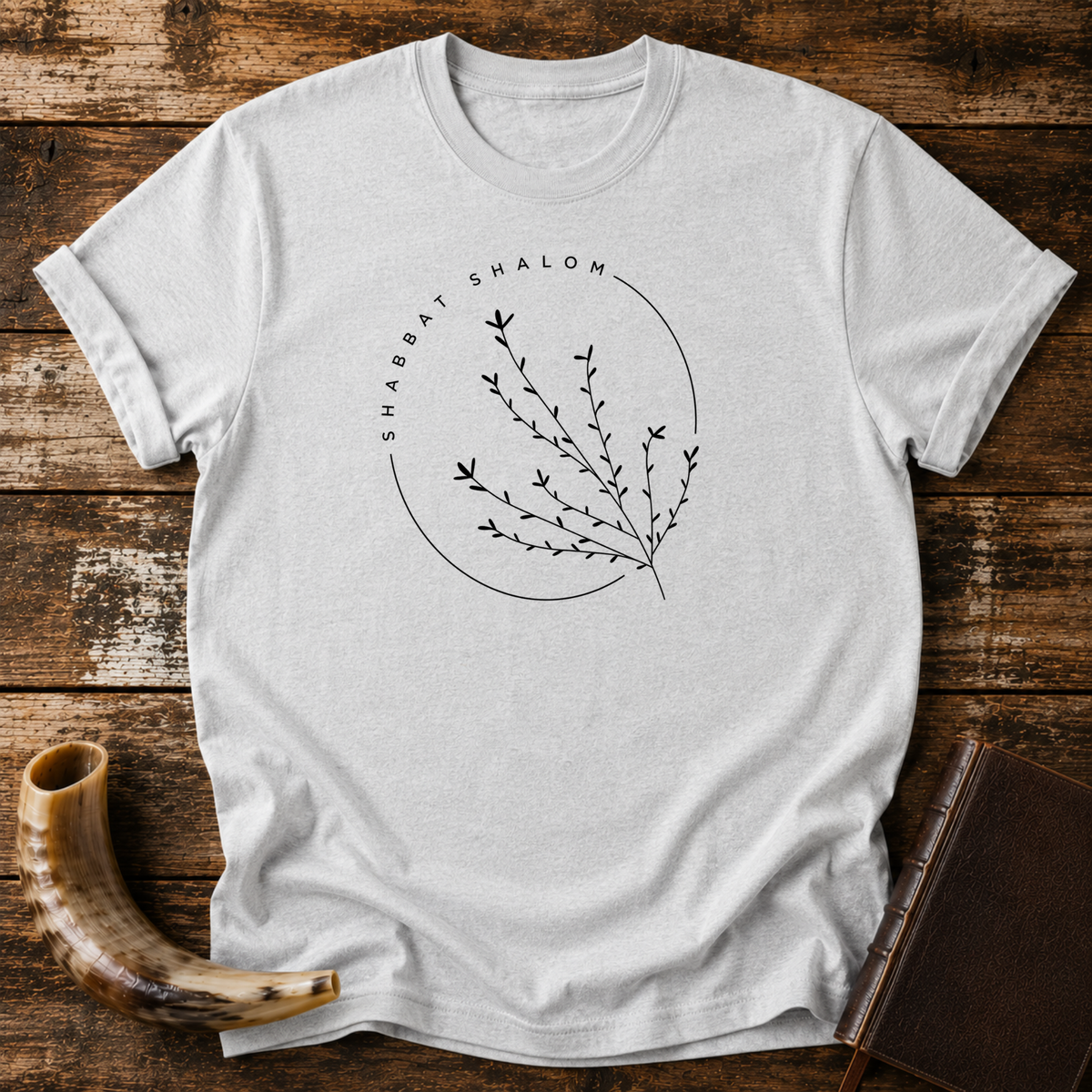 Sport grey t-shirt with a thin SHABBAT SHALOM circle around a delicate branch, laid flat with a shofar and a leather book