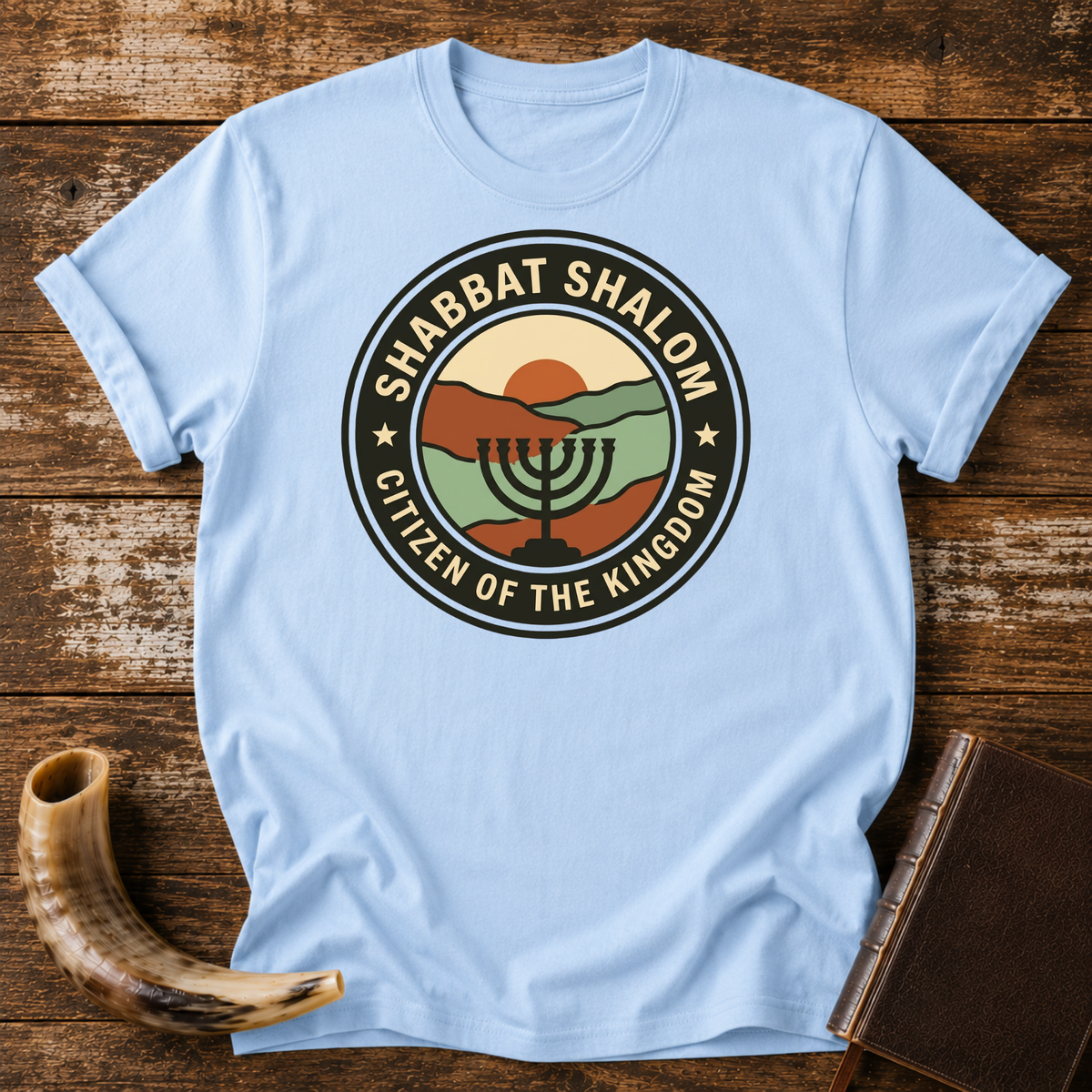 Light blue t-shirt with a SHABBAT SHALOM Citizen of the Kingdom badge with a menorah, laid flat with a shofar and a leather book