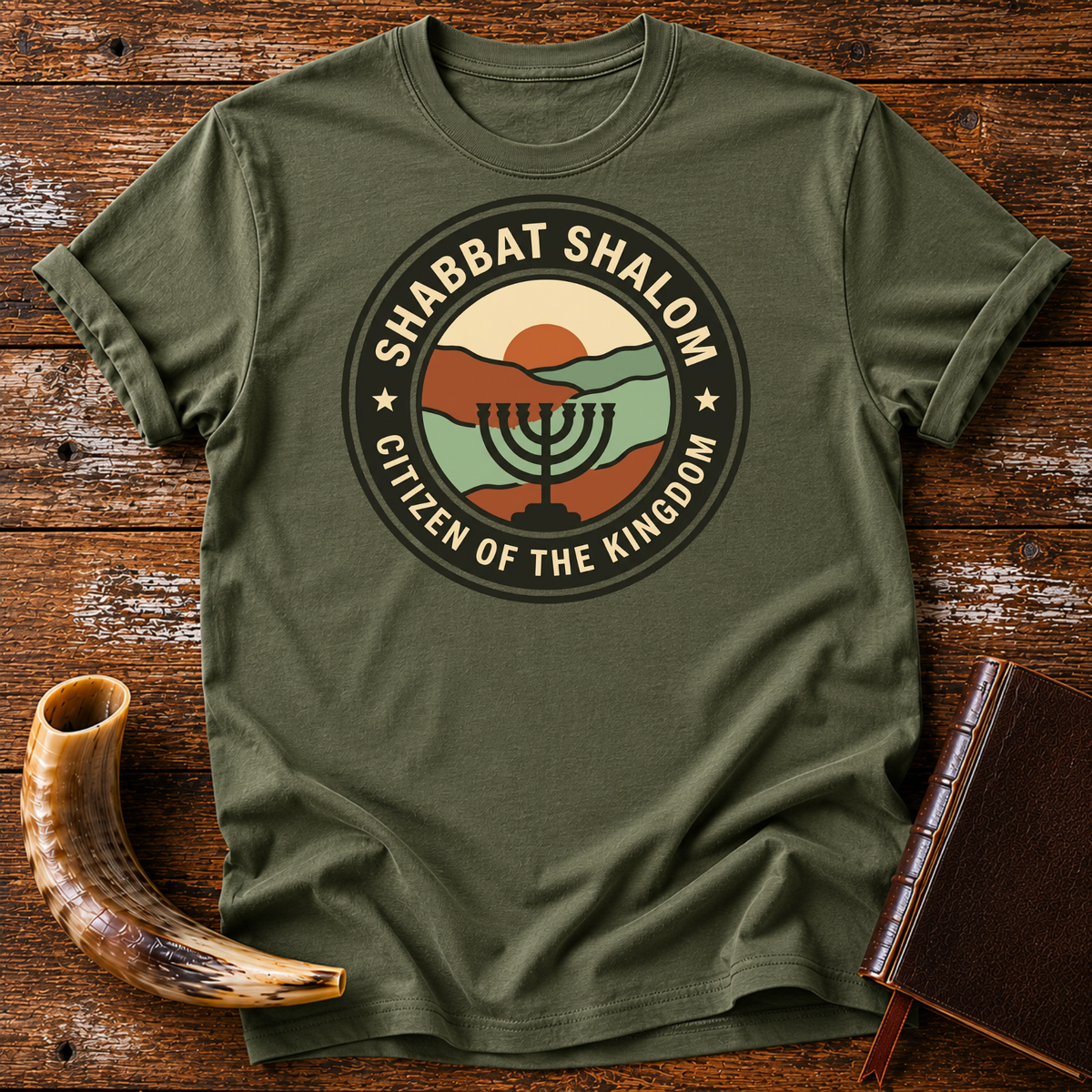 Military green t-shirt with a SHABBAT SHALOM Citizen of the Kingdom badge with a menorah, laid flat with a shofar and a leather book