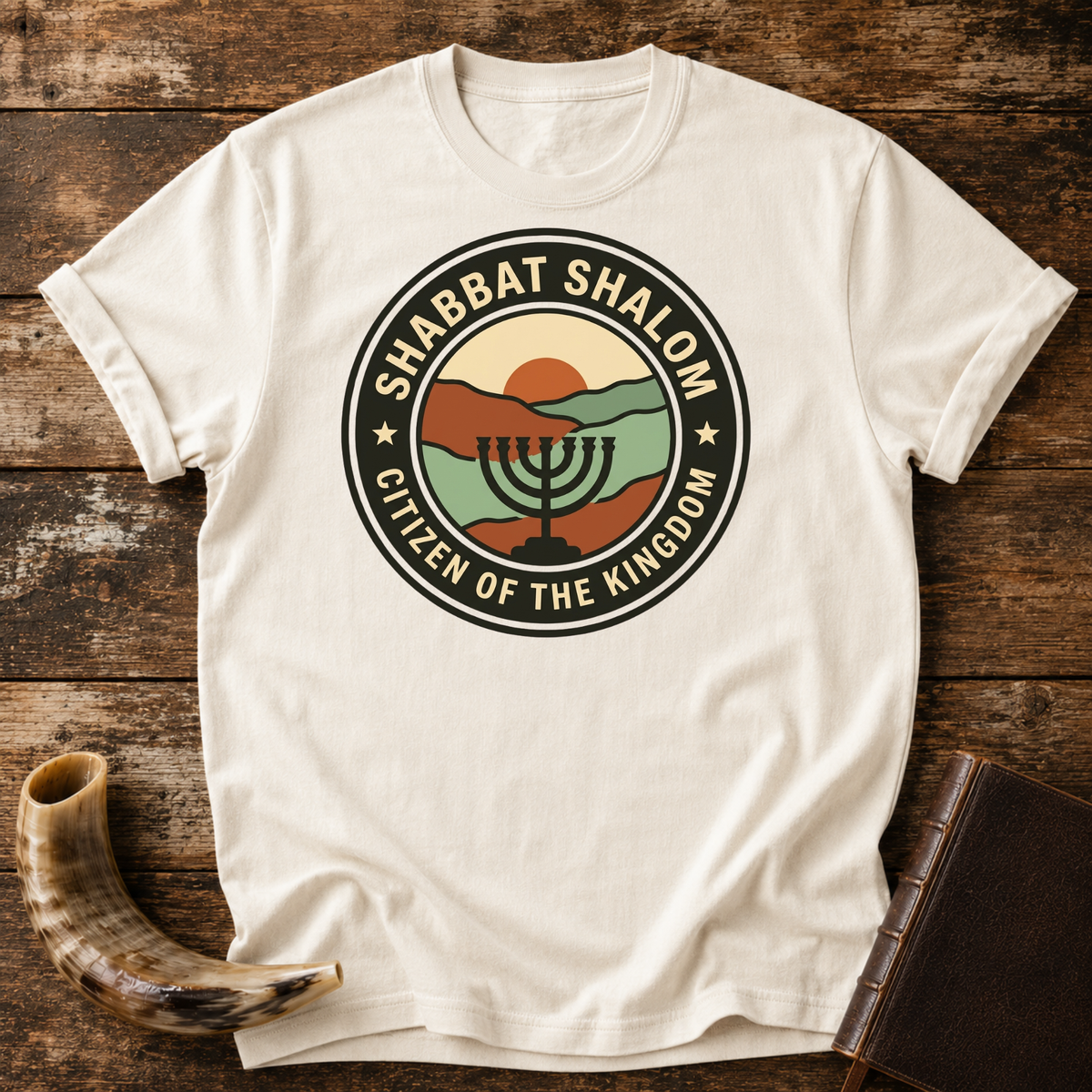 Natural cream t-shirt with a SHABBAT SHALOM Citizen of the Kingdom badge with a menorah, laid flat with a shofar and a leather book