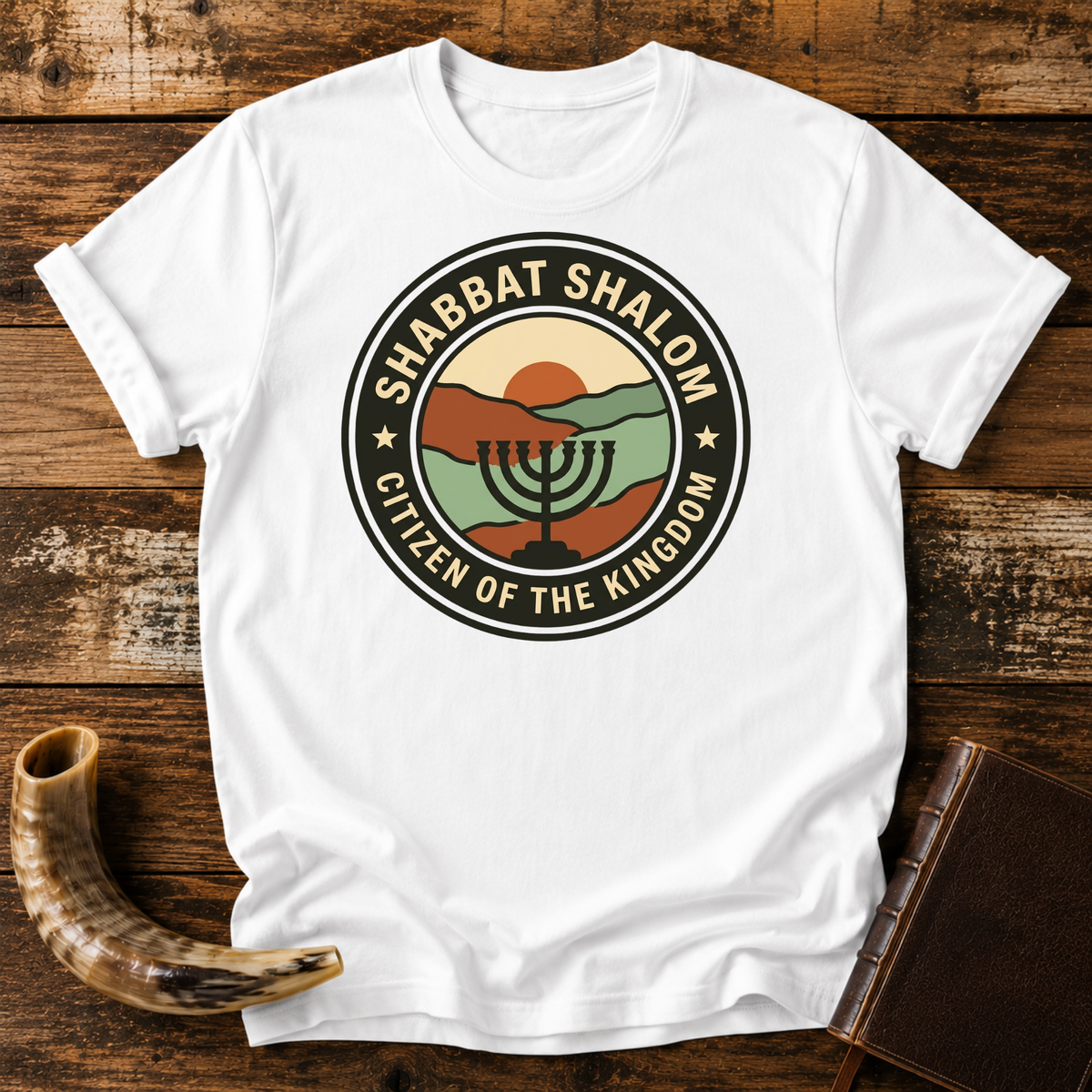 White t-shirt with a SHABBAT SHALOM Citizen of the Kingdom badge with a menorah, laid flat with a shofar and a leather book