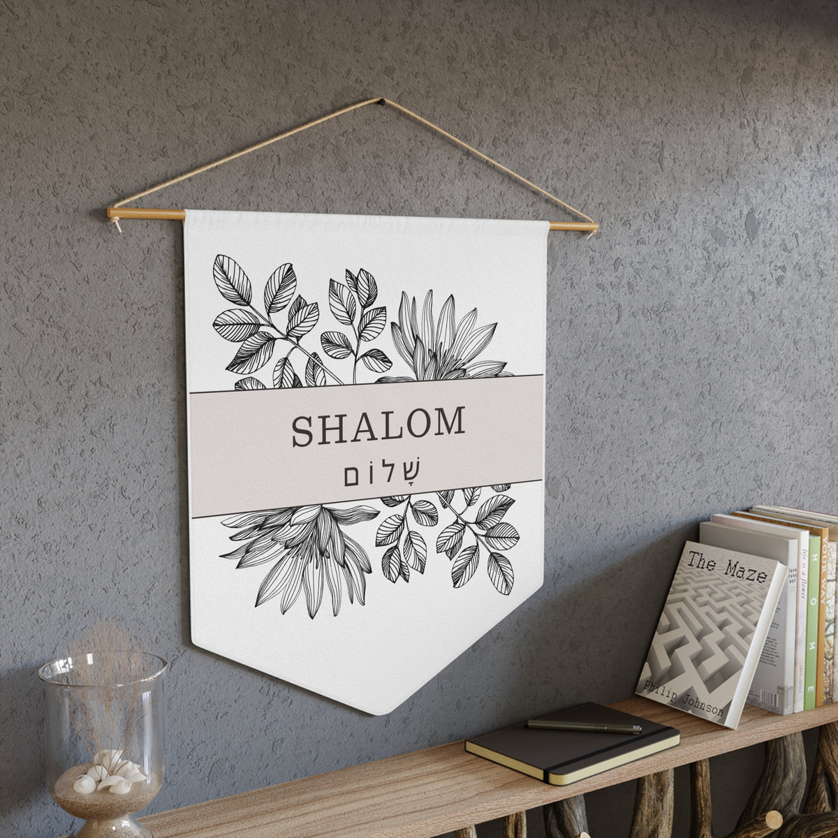 Shalom wall pennant with black botanical line art and "Shalom" in English and Hebrew, above a bookshelf