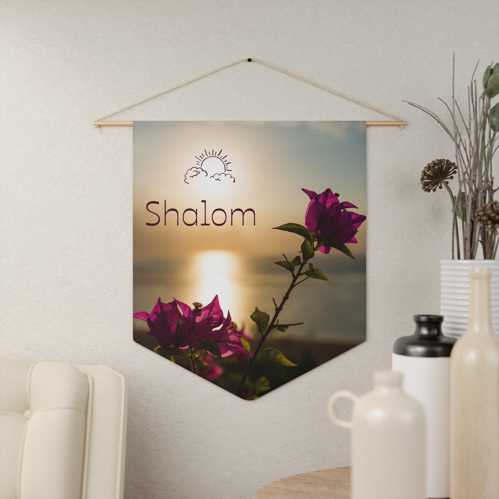 Shalom wall pennant with a sun icon, magenta bougainvillea and sunlight on water, hanging on a cream wall beside vases