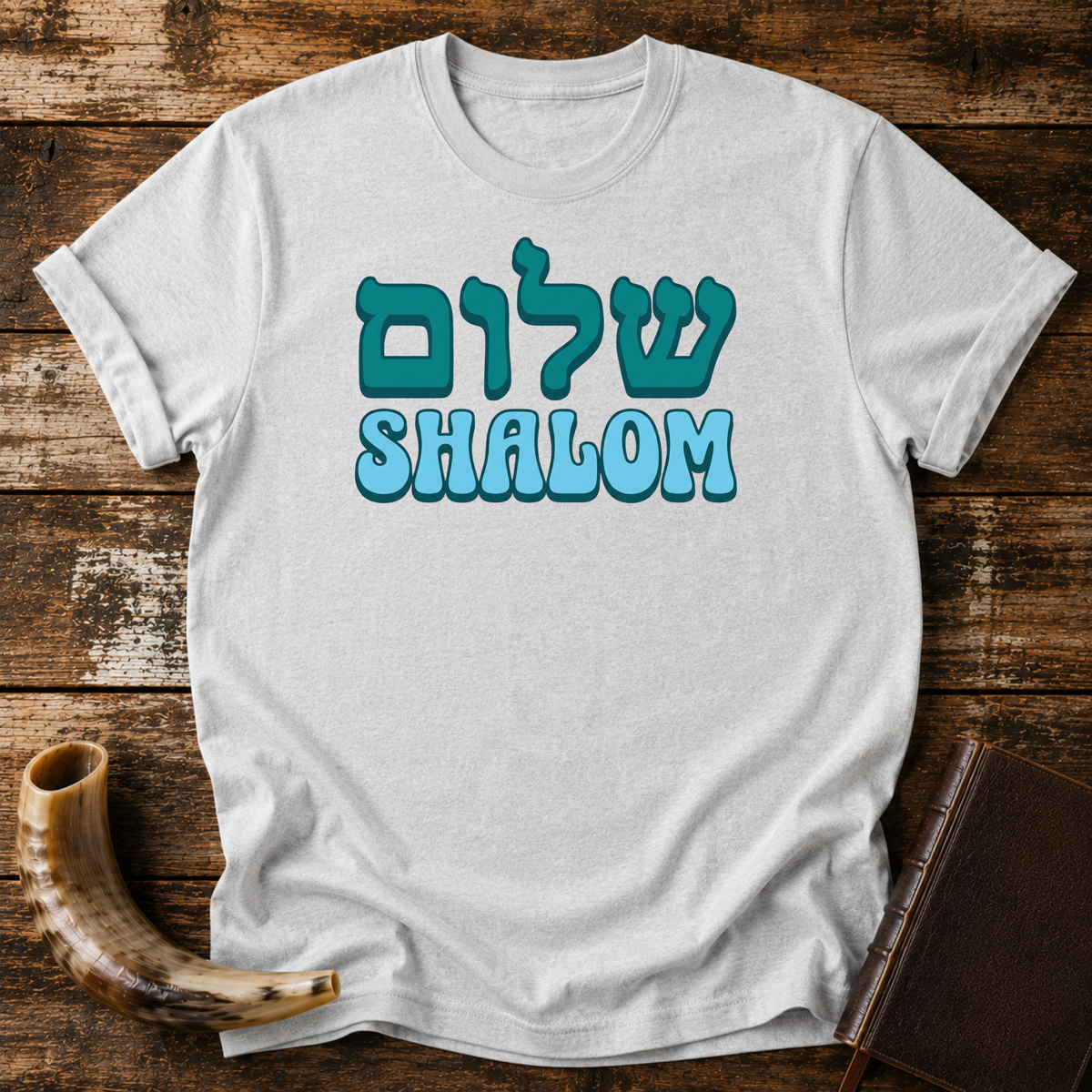 Sport grey t-shirt with teal Hebrew lettering above SHALOM in blue bubble letters, laid flat with a shofar and a leather book