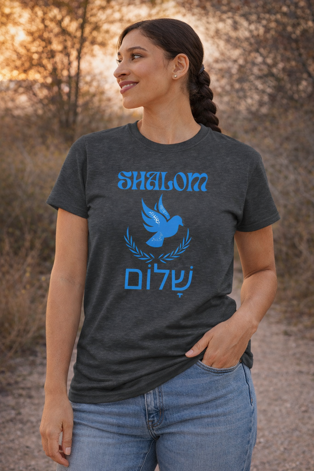 Dark heather Shalom dove t-shirt with a blue dove, laurel and Hebrew lettering, worn by a woman outdoors