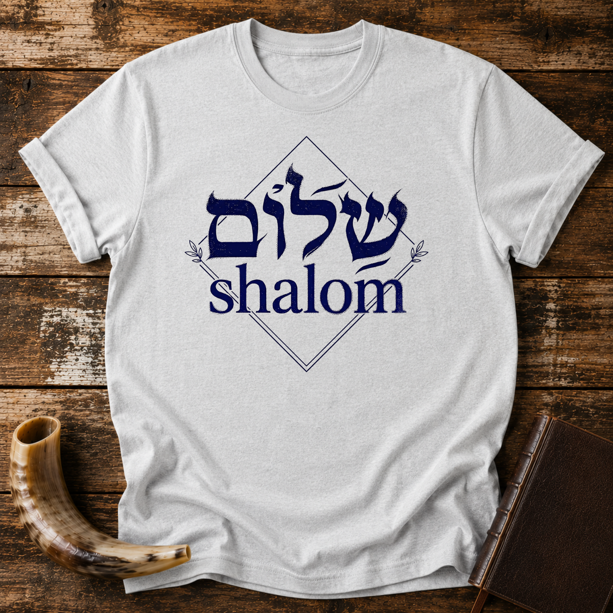 Sport grey t-shirt with navy Hebrew lettering and the word shalom inside a diamond outline, laid flat with a shofar and a leather book