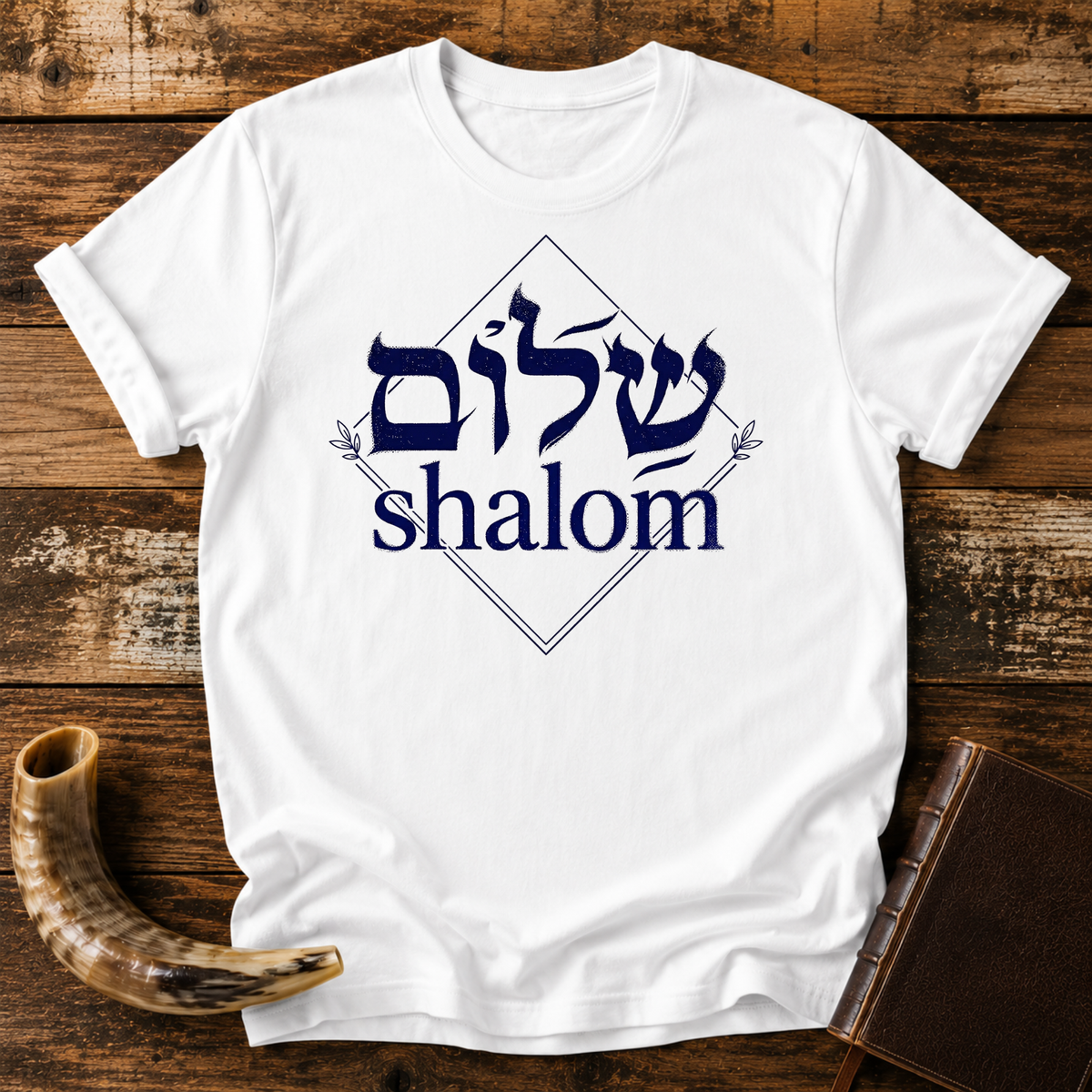 White t-shirt with navy Hebrew lettering and the word shalom inside a diamond outline, laid flat with a shofar and a leather book
