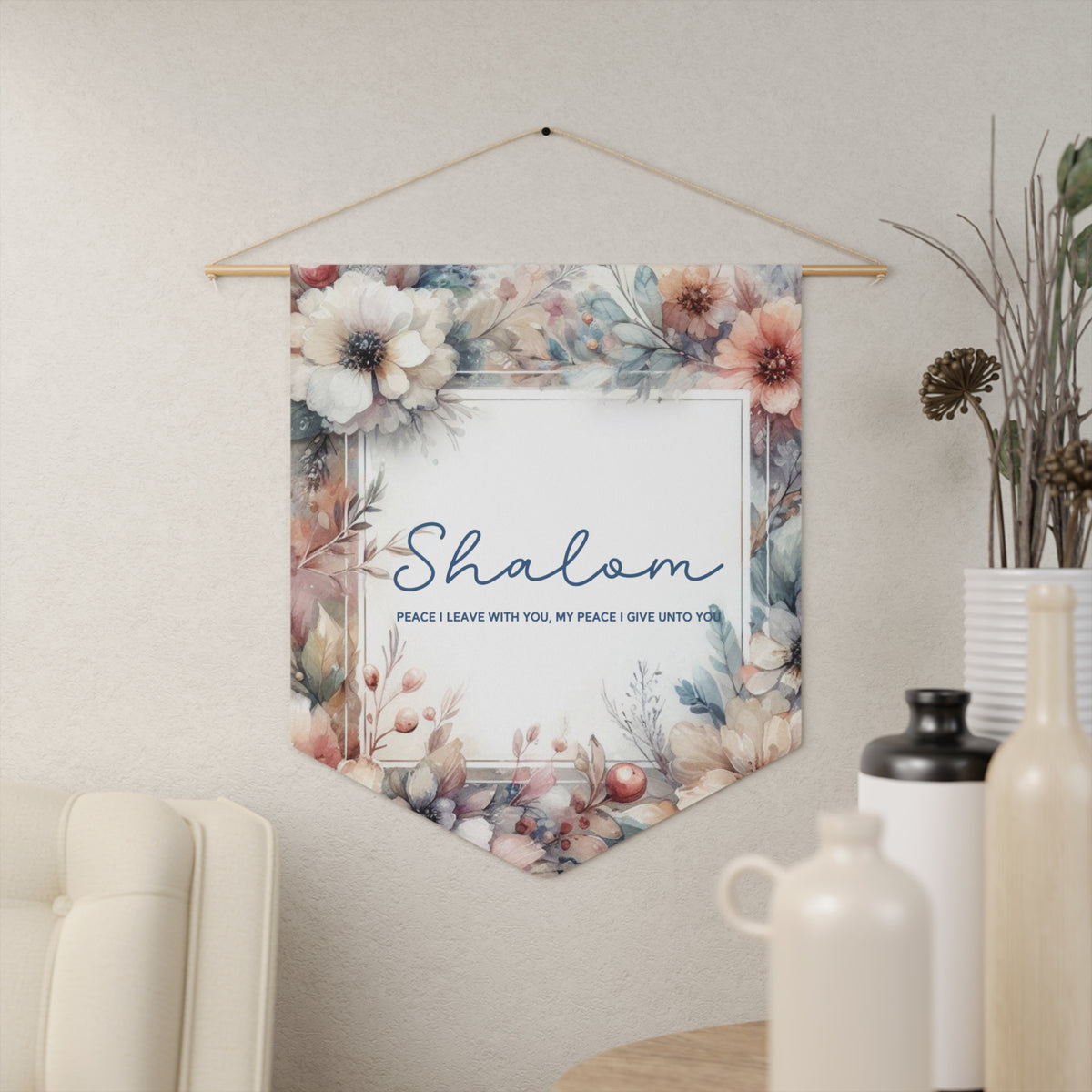 Shalom wall pennant framed in watercolor flowers with Peace I leave with you, my peace I give unto you, hanging on a cream wall beside vases