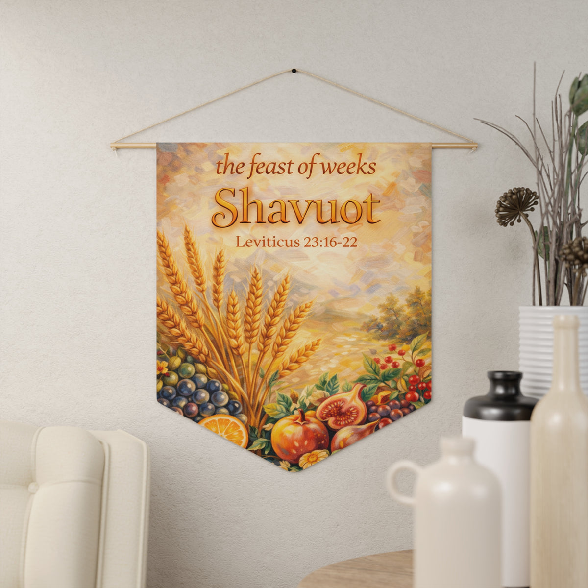 Golden feast of weeks Shavuot wall pennant with wheat sheaves, pomegranates and grapes, Leviticus 23:16-22, hanging on a cream wall beside vases