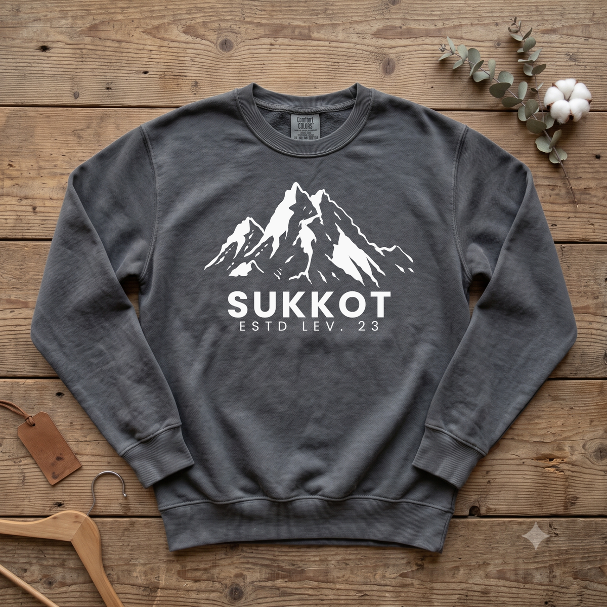 Pepper gray Sukkot ESTD Lev. 23 sweatshirt with a white mountain peak graphic, laid flat on wood boards