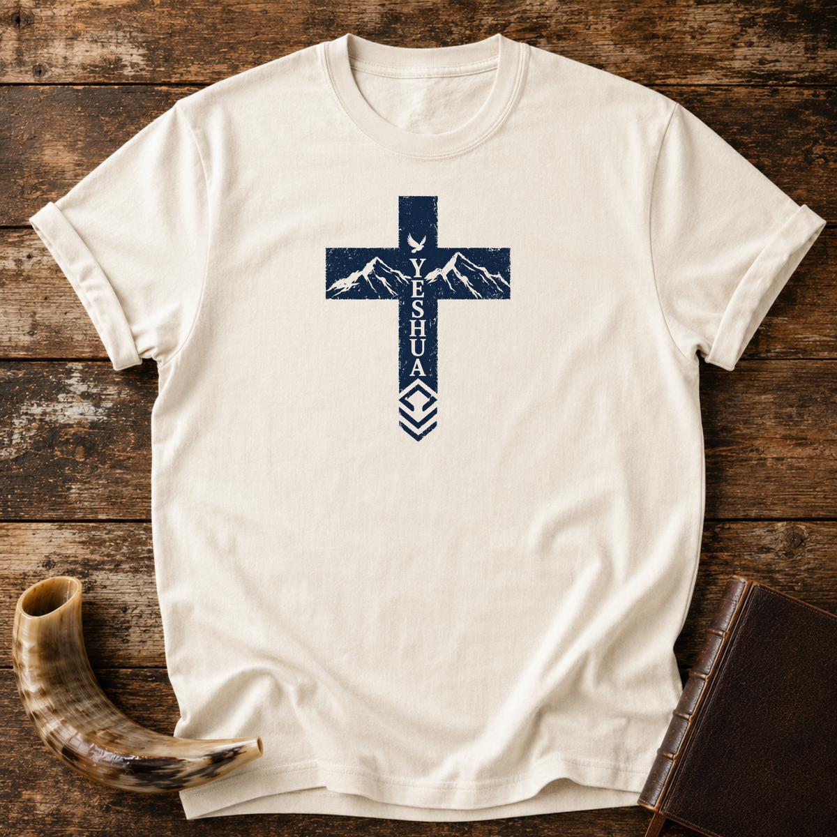 Natural Yeshua cross t-shirt with mountains and a dove in the cross, laid flat with a shofar and Bible