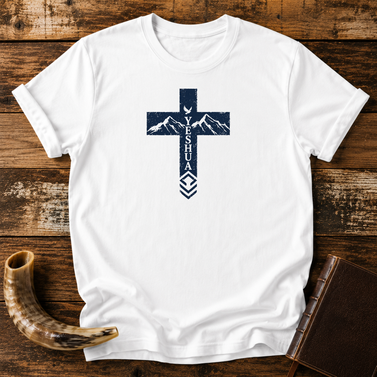 White Yeshua cross t-shirt with mountains and a dove in the cross, laid flat with a shofar and Bible