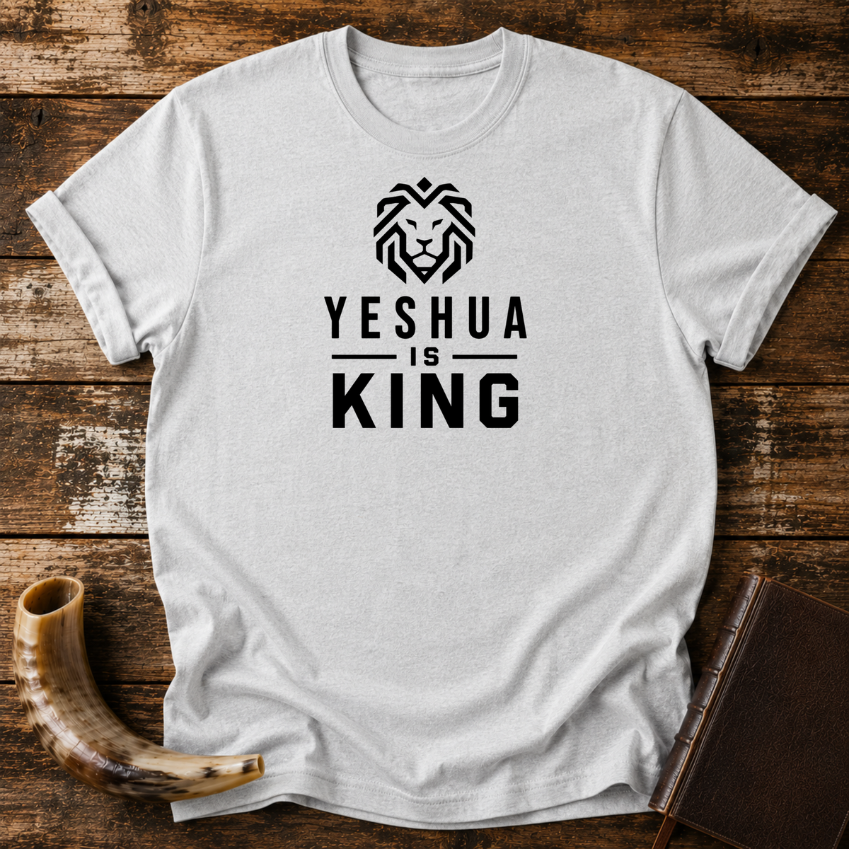 Sport grey t-shirt with a geometric lion head above YESHUA IS KING lettering, laid flat with a shofar and a leather book