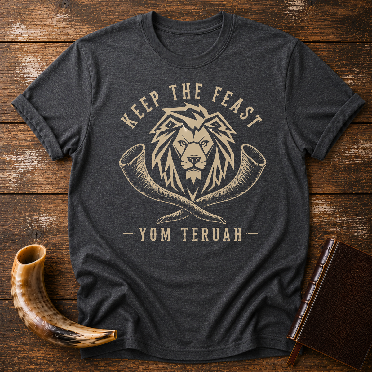 Dark heather gray t-shirt with a tan lion head over crossed shofars, KEEP THE FEAST YOM TERUAH, laid flat with a shofar and a leather book