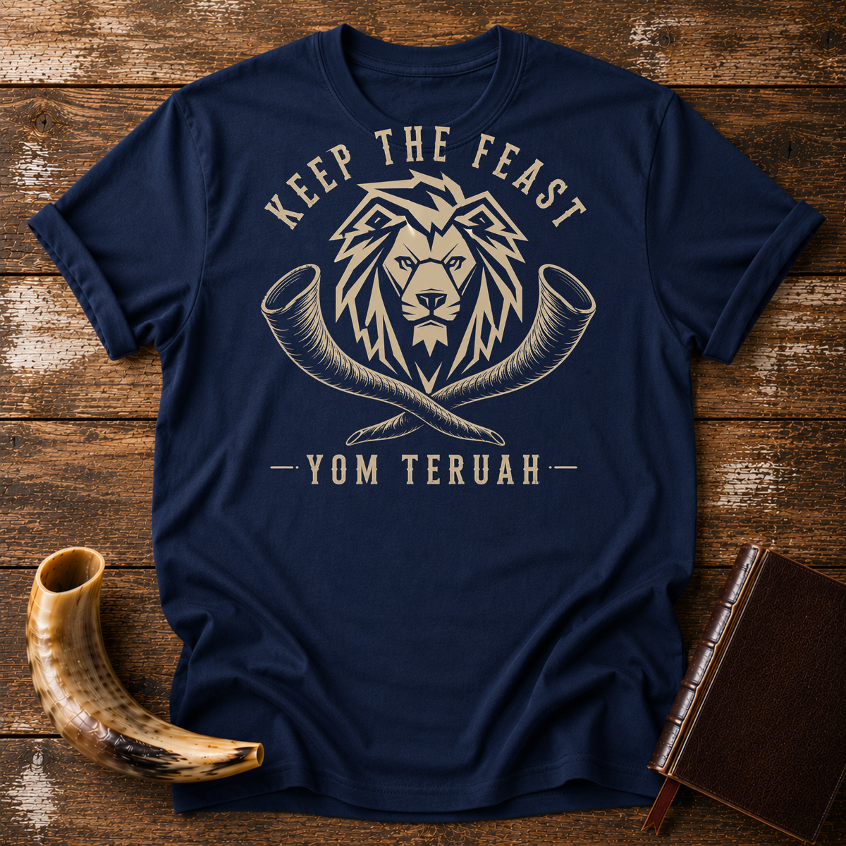 Navy t-shirt with a tan lion head over crossed shofars, KEEP THE FEAST YOM TERUAH, laid flat with a shofar and a leather book