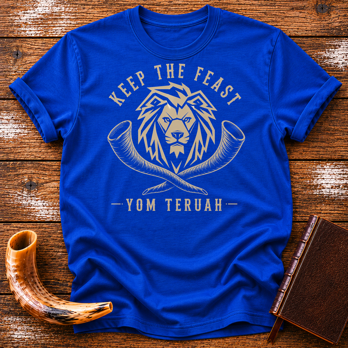 Royal blue t-shirt with a tan lion head over crossed shofars, KEEP THE FEAST YOM TERUAH, laid flat with a shofar and a leather book