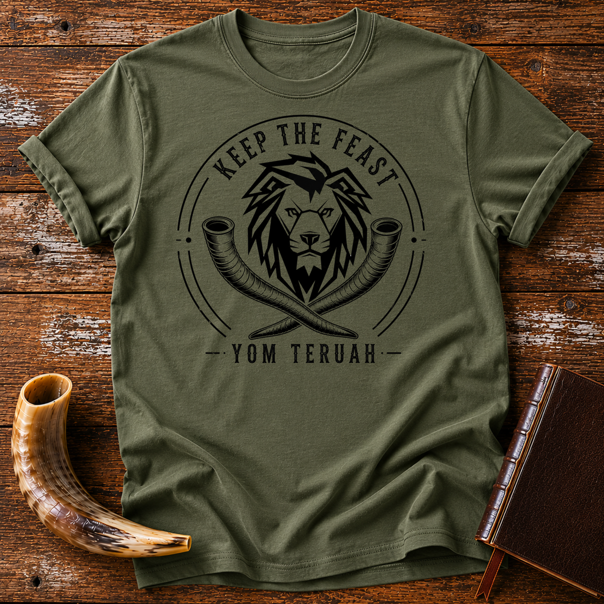 Military green t-shirt with a black lion head over crossed shofars, KEEP THE FEAST YOM TERUAH, laid flat with a shofar and a leather book